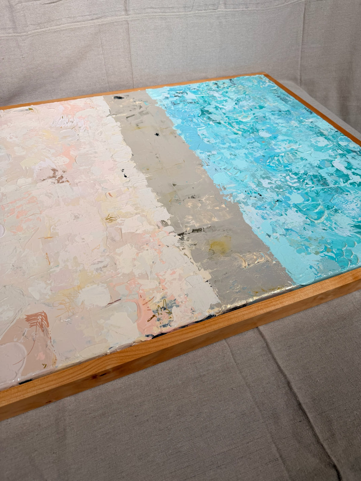Angled close-up of The Money Keeps Us Divided showing crackled blush-pink texture, a gold dividing band and mottled turquoise in a wood frame.