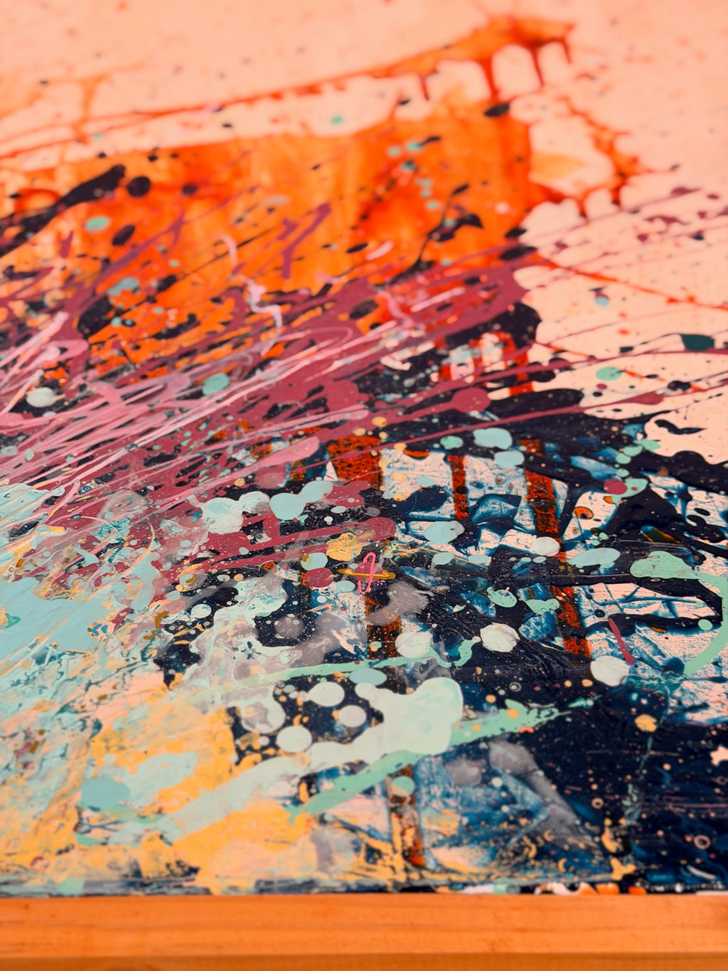 Close-up of I Have My Own Gravity: thick orange paint over a dense spray of navy, rose and cream drips near the wood frame.