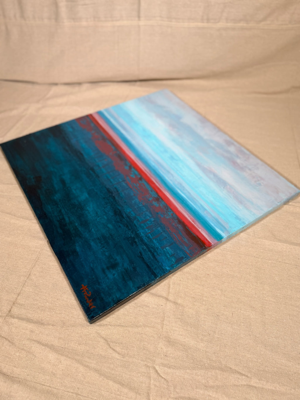 Rest in Your Peace lying at an angle on canvas cloth, showing the textured teal sea, coral horizon line and pale sky bands.