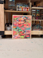 Pretty Girls Walk leaning against a studio supply shelf full of paints: a framed burst of coral, pink, teal and lime textured paint.