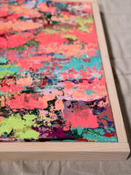 Angled close-up of Pretty Girls Walk showing heavily textured coral, hot pink, turquoise and lime paint inside a light wood frame.