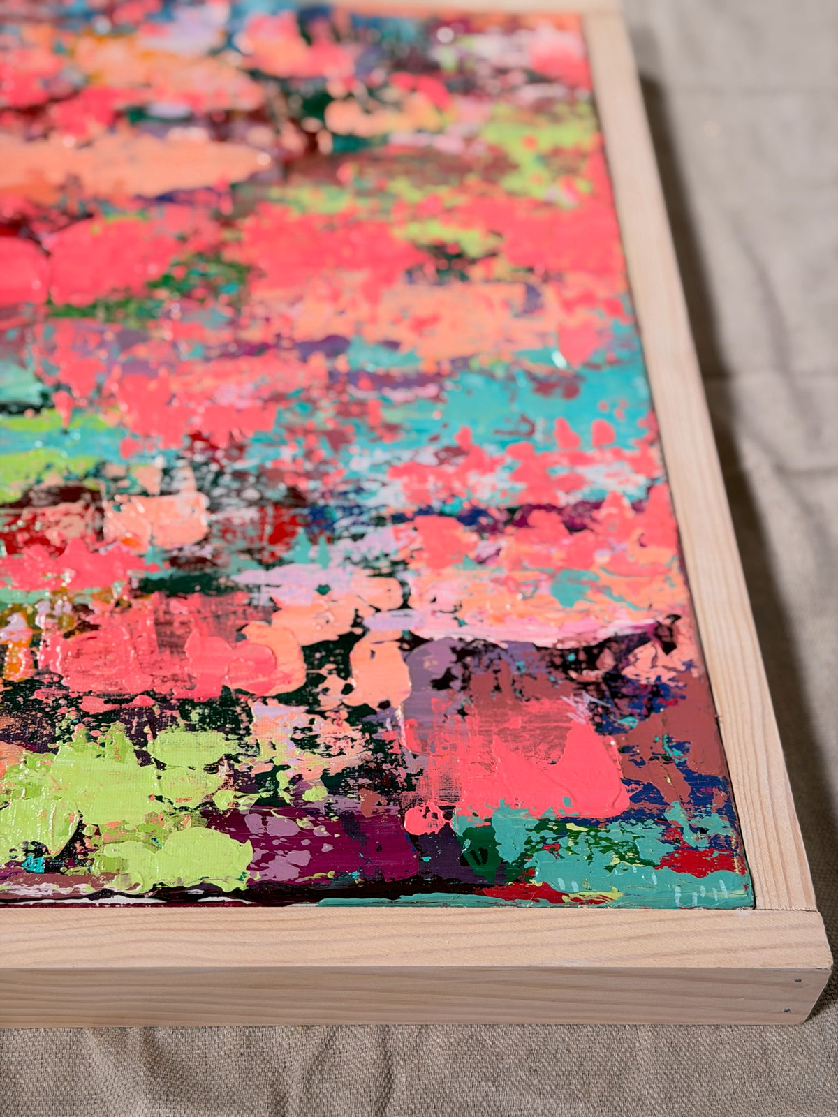 Angled close-up of Pretty Girls Walk showing heavily textured coral, hot pink, turquoise and lime paint inside a light wood frame.