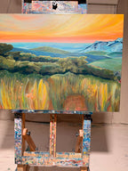 By Way Of The Weeds on a paint-splattered easel, viewed straight on: sunset sky, pale blue distant mountains, dark green trees and textured golden weeds.