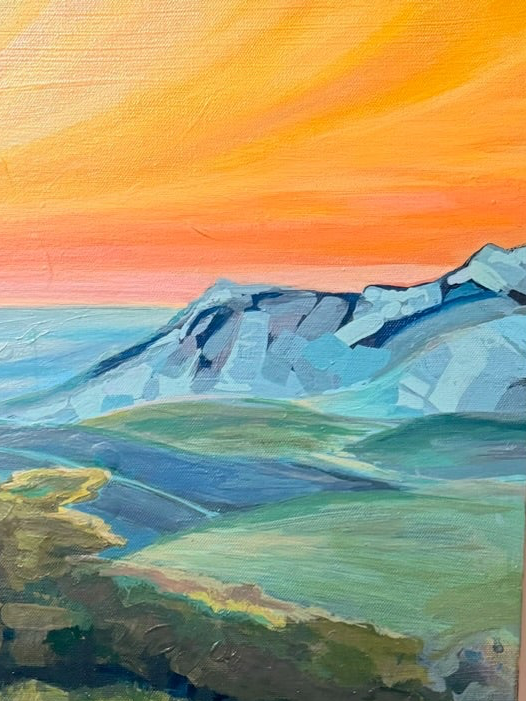 Close-up of By Way Of The Weeds: a blazing orange and gold sky meets icy blue, faceted mountains above soft green hills.