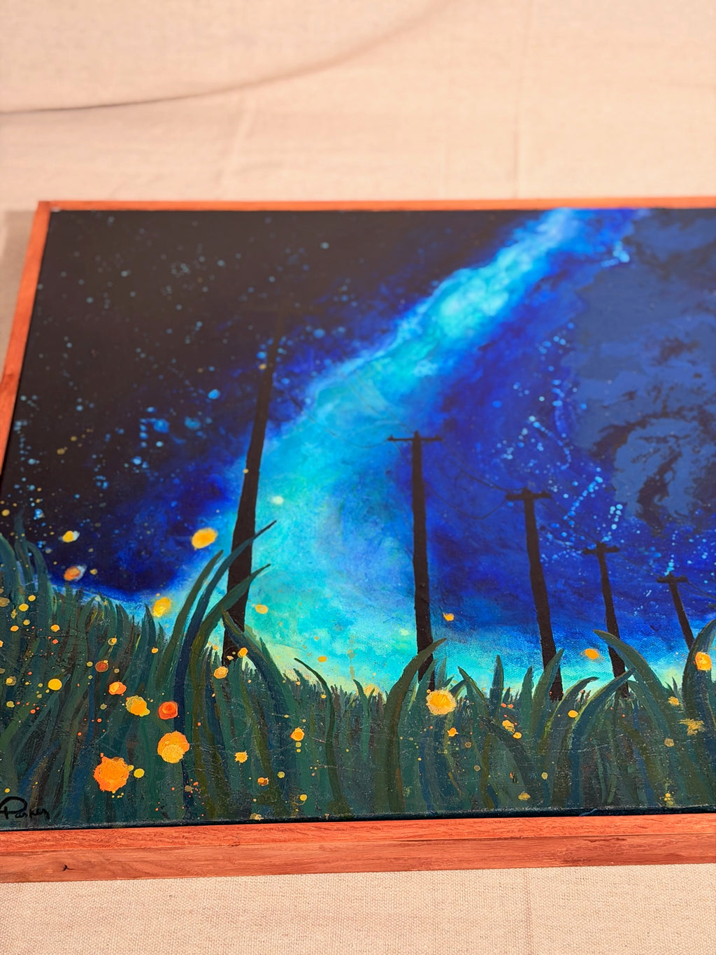 Angled close-up of The View From The Grass: a bright blue starry sky streaks above tall dark grass, slim poles and dots of glowing orange fireflies.