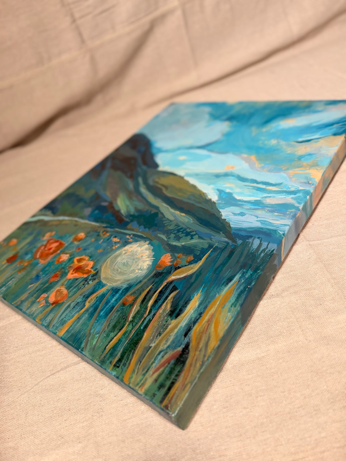 Angled close-up of My Once Obliterated Self-Esteem showing textured teal grasses, orange poppies and a glowing white dandelion seed head.