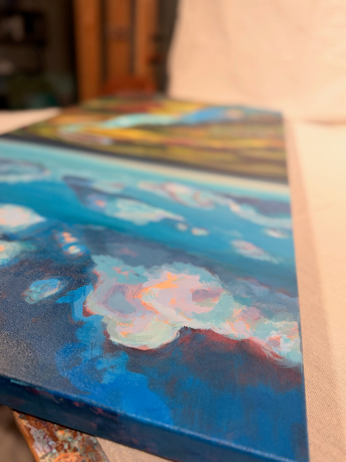 Angled close-up of the top of Where the Cahaba Winds, showing soft white and pink clouds on a deep blue sky and the painted canvas edge.