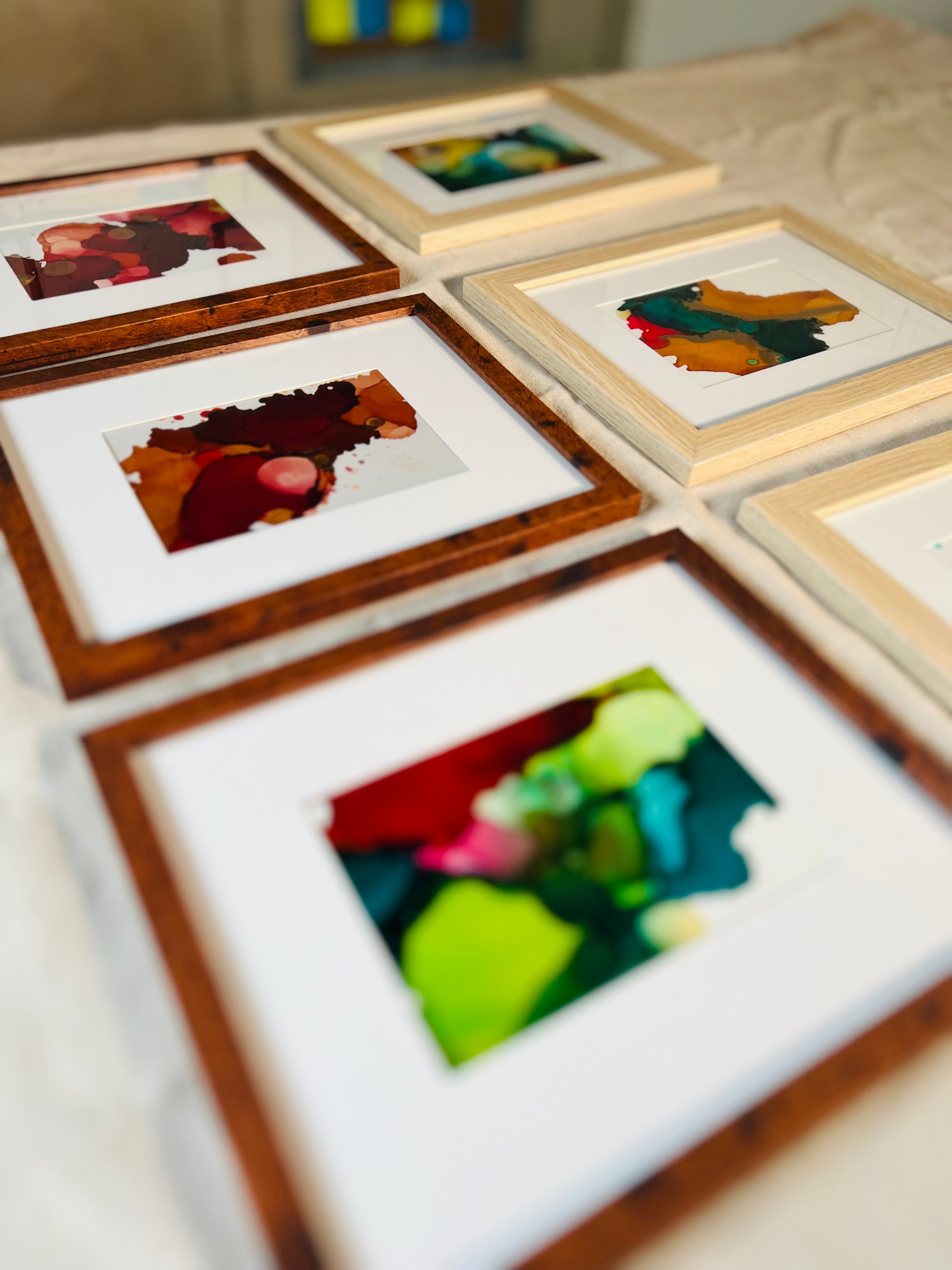 Several of Kindra Knight Parker's small colorful abstract artworks in white mats and warm wood frames, laid out together on a table.