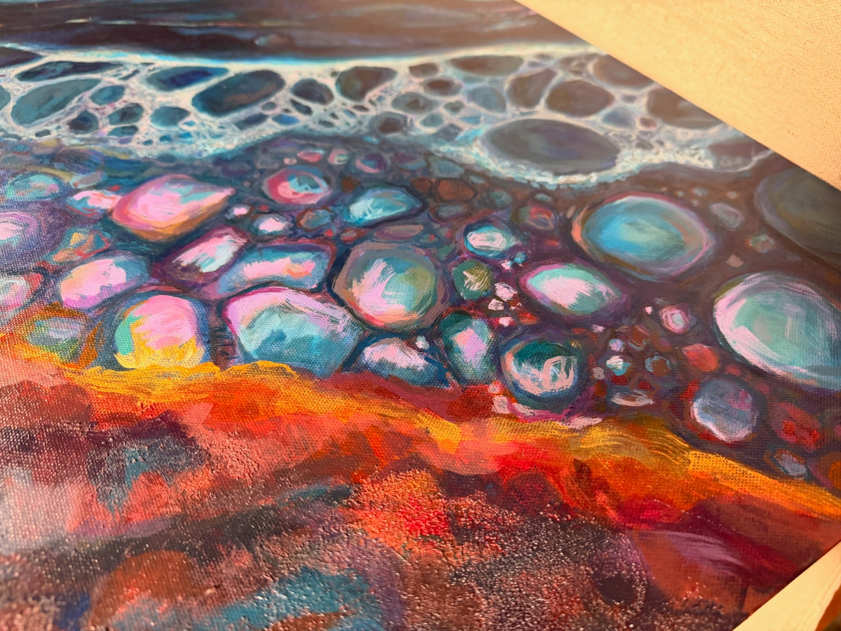 Close-up of Polished By The Rough Torrent: shiny turquoise, pink and lilac pebble shapes laced with white foam above textured red-orange.