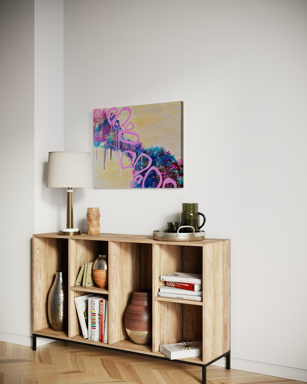 Beautiful Mess hanging above a light wood bookshelf with a lamp and pottery in a simple, bright room.
