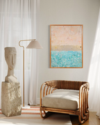 The Money Keeps Us Divided hanging in a sunny corner above a rattan chair beside a stone face sculpture and floor lamp.
