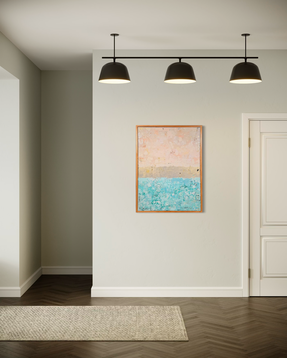 The Money Keeps Us Divided shown on a pale wall in a hallway beneath black pendant lights, its blush, gold and turquoise bands framed in wood.