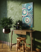 Presence, a tall abstract in mixed media on stretched canvas of overlapping teal, cream and rose ripple circles, shown on a green plaster wall above a wooden desk.