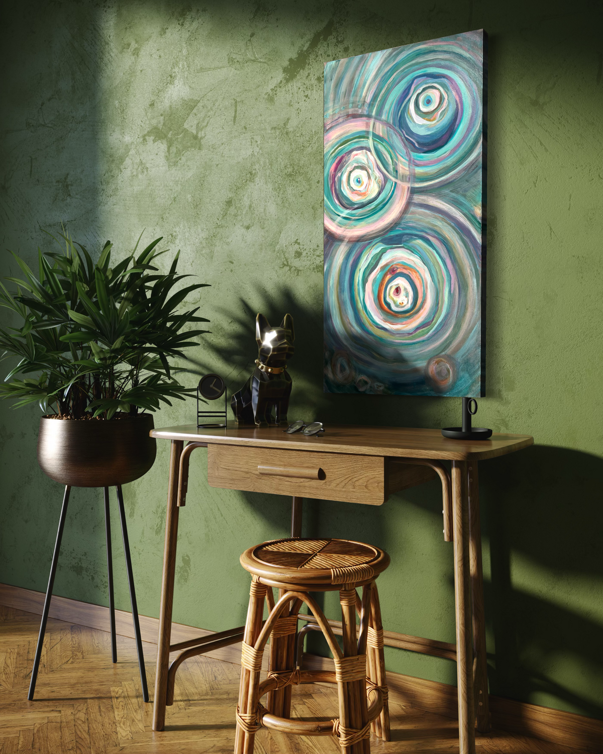 Presence, a tall abstract in mixed media on stretched canvas of overlapping teal, cream and rose ripple circles, shown on a green plaster wall above a wooden desk.