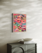 Pretty Girls Walk hanging on a sunlit plaster wall above a dark gray cabinet, its bright coral and turquoise texture framed in light wood.