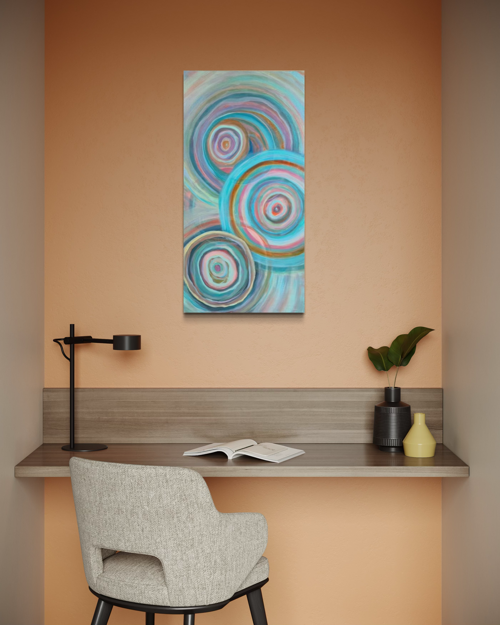 Abundance, a tall abstract in mixed media on stretched canvas of concentric ripple circles in turquoise, pink, cream and copper, shown above a desk in a peach-walled nook.