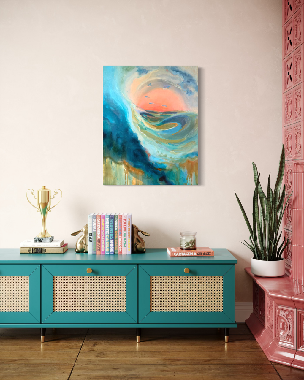 As The Path Unfolds displayed above a teal rattan sideboard with books and a trophy, its swirling blue wave framing a glowing coral sun.
