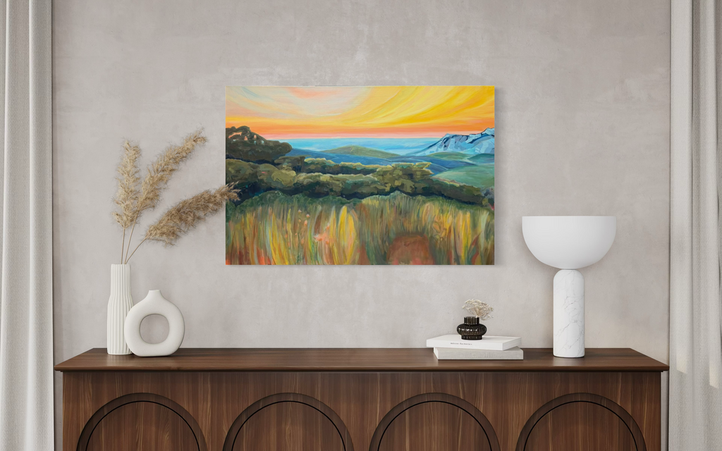 By Way Of The Weeds displayed above a dark wooden sideboard with white vases, showing golden grasses and green hills beneath a bright yellow sky.