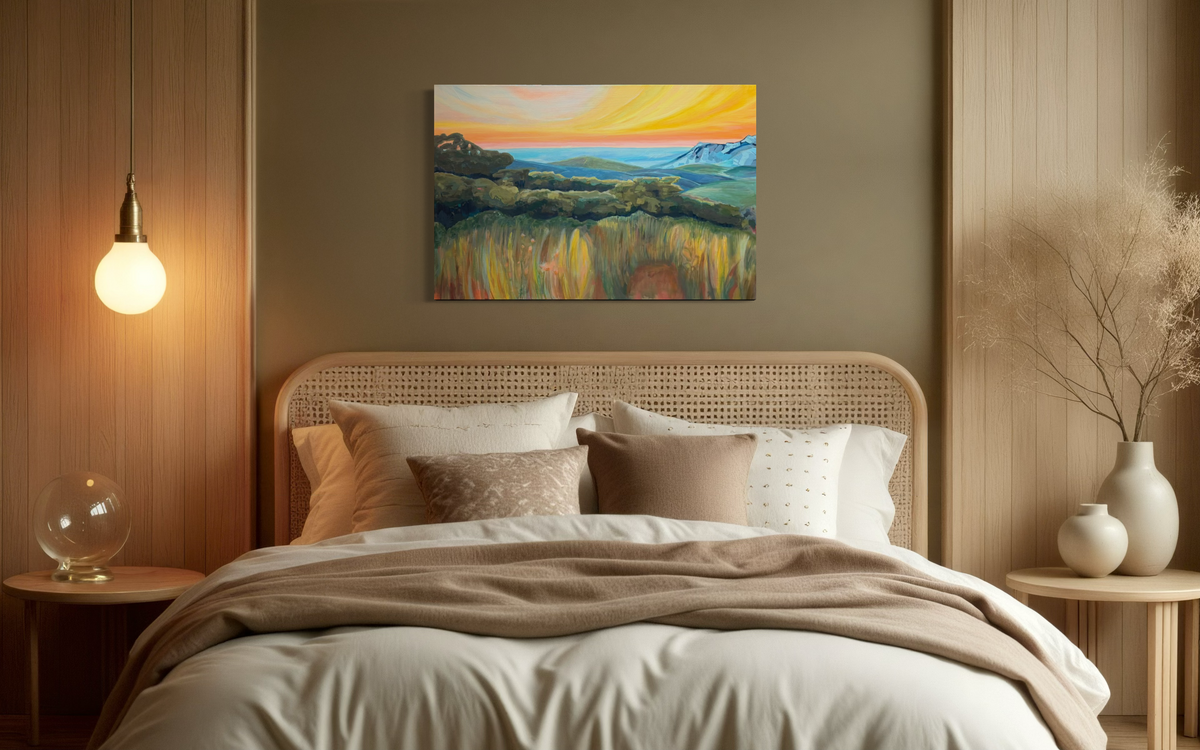 By Way Of The Weeds shown above a cream bed in a warm bedroom with a woven headboard, its orange sky and golden meadow adding a sunset glow.