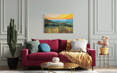 By Way Of The Weeds, a landscape in mixed media on stretched canvas: tall golden grasses and green hills under a glowing orange and yellow sunset, shown above a magenta sofa.