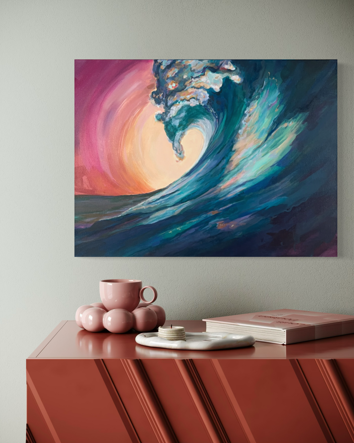 Held In The Current, in mixed media on stretched canvas: a curling teal and navy wave against a glowing pink and peach sun, shown above a terracotta sideboard.