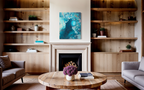 Suspended In The Swell, an abstract in mixed media on stretched canvas of deep teal water filled with pale aqua bubbles, shown above a fireplace with wooden shelves.