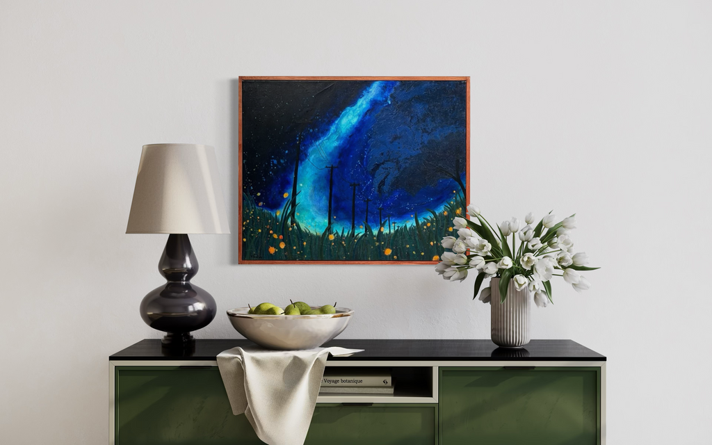 The View From The Grass hanging above a green sideboard with a lamp and white tulips: a turquoise Milky Way arcs over a dark meadow dotted with fireflies.