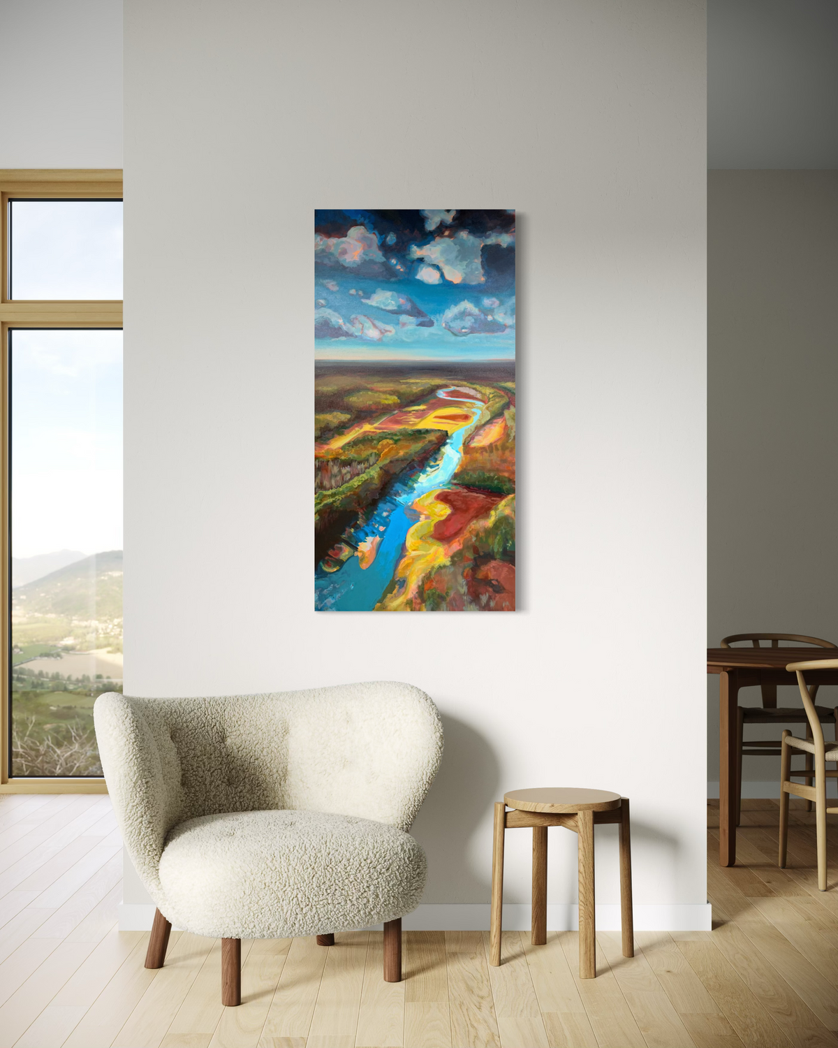 Where the Cahaba Winds shown in a bright living room above a cream bouclé armchair and wooden stool. A blue river snakes through colorful land beneath puffy clouds.