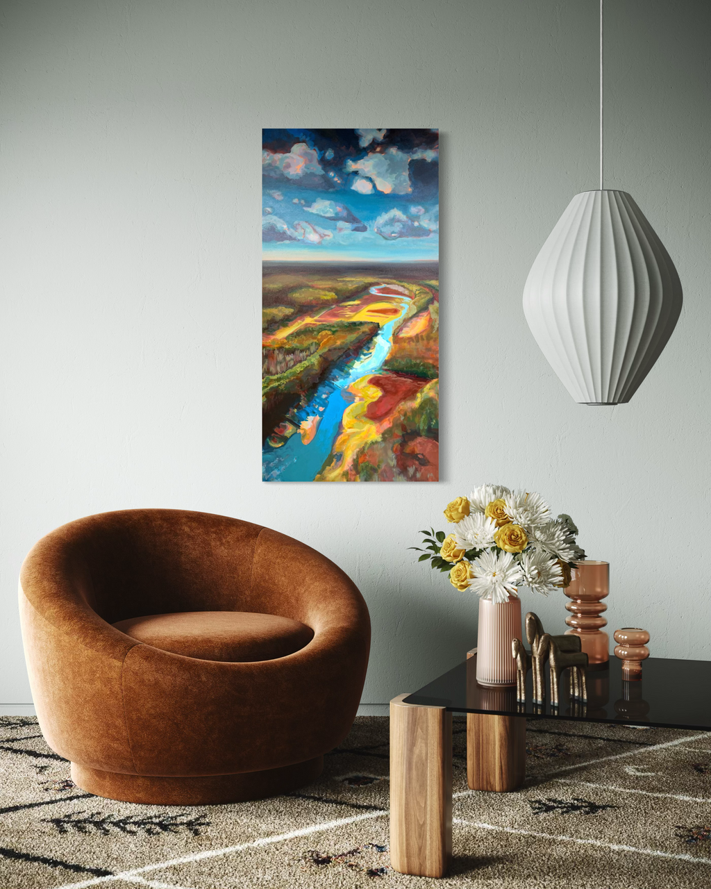 Where the Cahaba Winds displayed in a modern lounge above a rust velvet chair and glass coffee table, showing a river winding from a cloudy blue sky through vivid land.